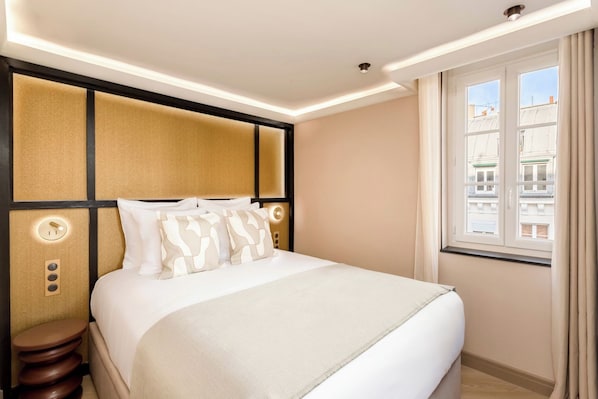 A hotel room with a bed, bedside table, and a window with curtains. - Merveil - Signature Suite - Louvre - Bourse II (Paris)