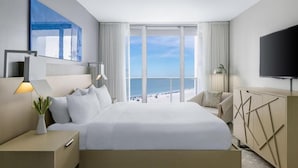 Une chambre d’hôtel moderne dotée d’un grand lit, d’une télévision, d’un bureau et offrant une vue sur la plage.