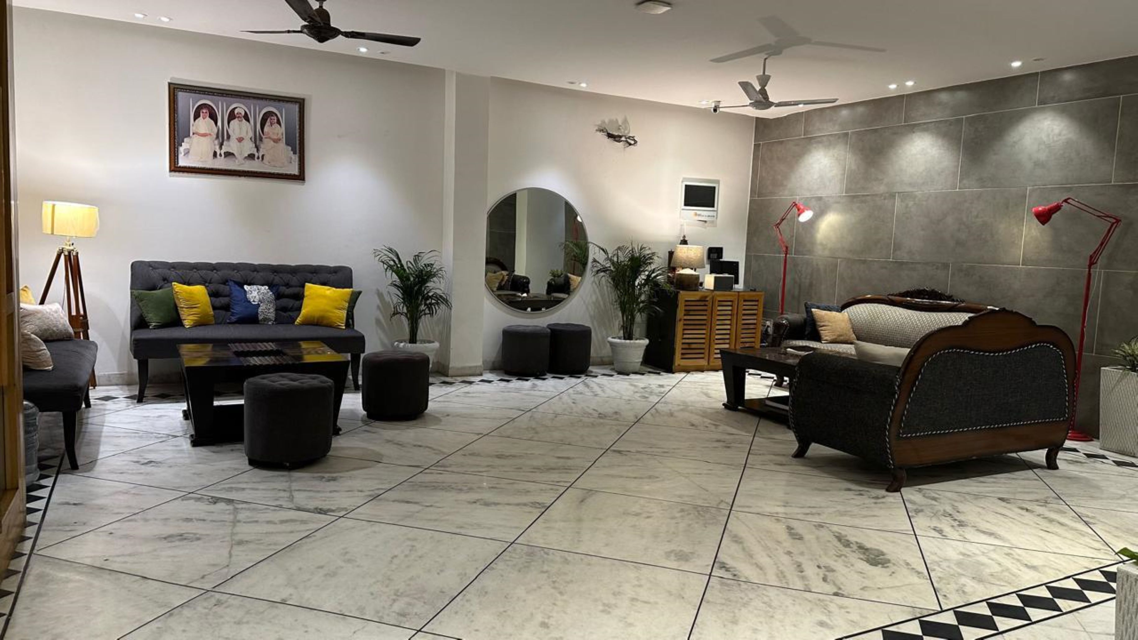 A modern living room with a sofa, armchairs, a coffee table, and a TV. There is a large mirror, a ceiling fan, and a potted plant.