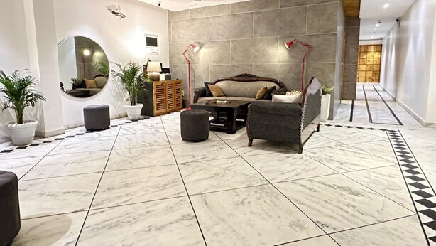 Un vaste espace de vie comprenant un grand canapé, des poufs et une table basse. Un grand miroir rond est accroché au mur, ainsi qu’une plante en pot et un ventilateur de plafond.