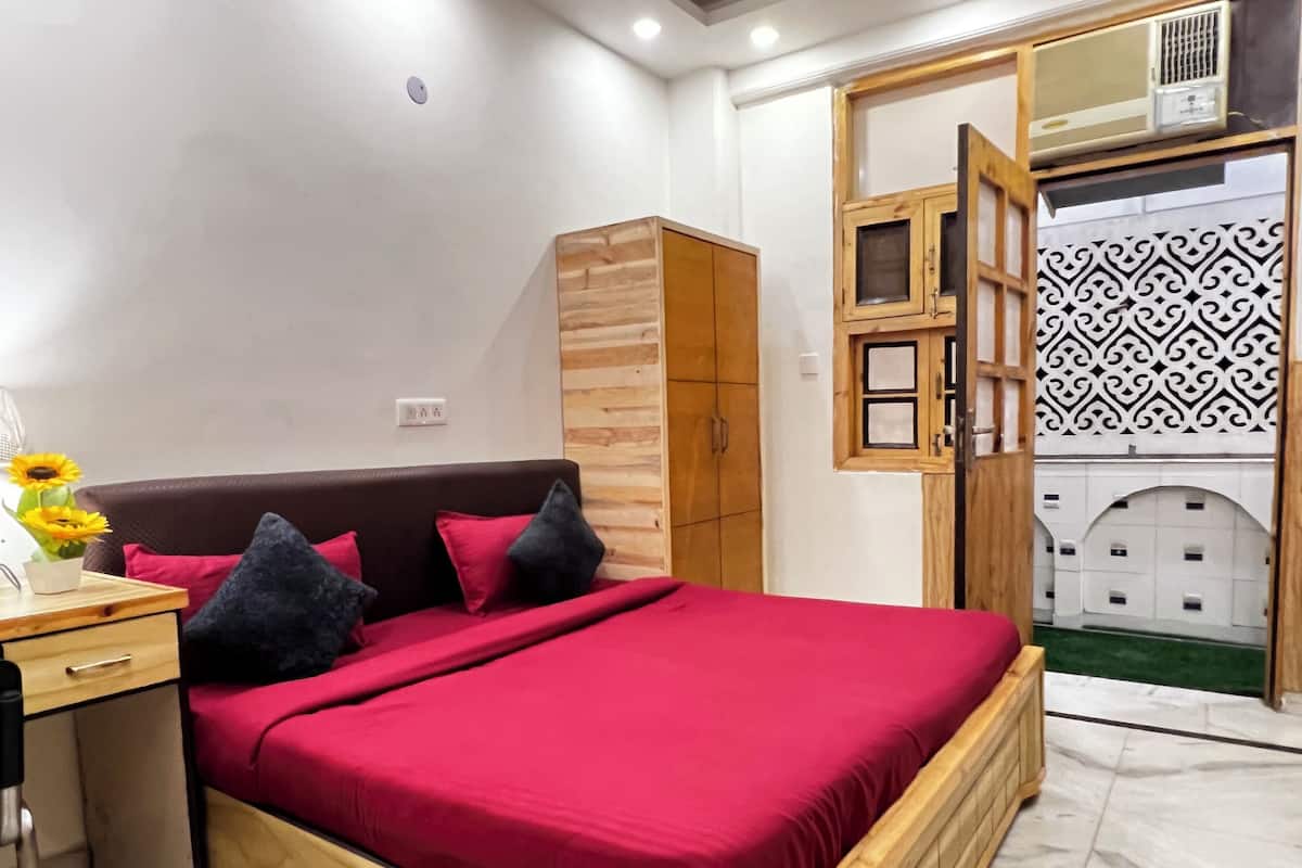 Quarto com estrutura de cama de madeira, roupa de cama vermelha, guarda-roupa de madeira e um painel decorativo na parede.