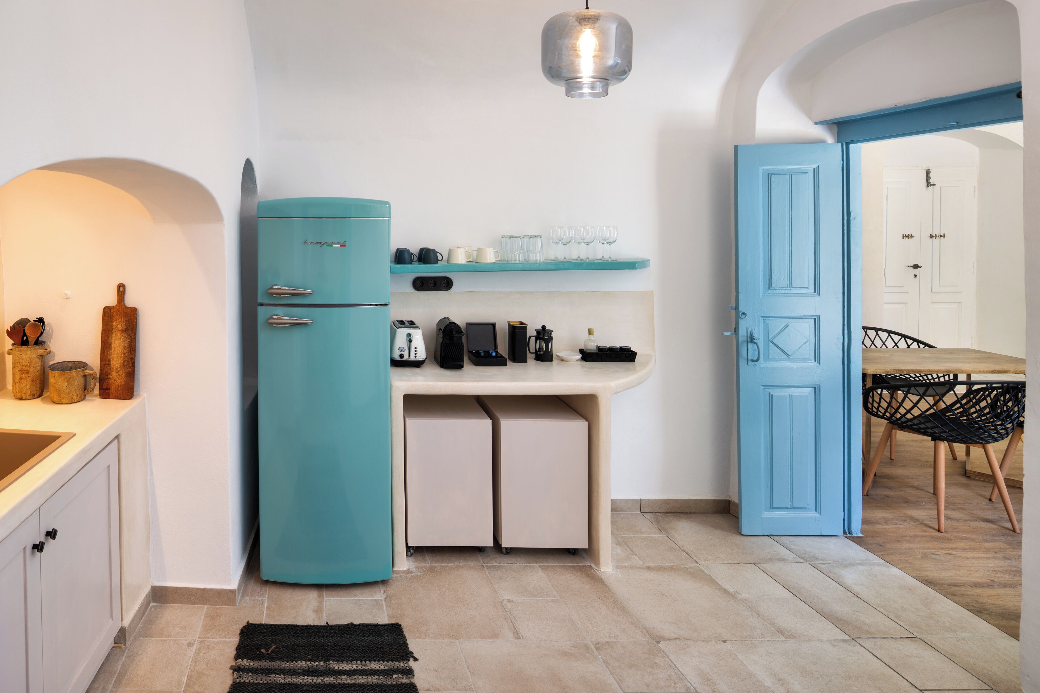 A compact kitchen with a teal refrigerator, a countertop with various appliances, and a dining area with a table and chairs.