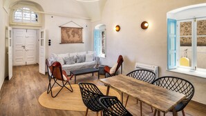 A cozy interior with a wooden dining table, black wireframe chairs, a sofa, and a hanging light fixture.