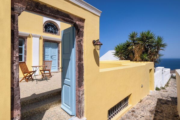 A yellow building with a blue door, a small patio with chairs, and a view of the sea.