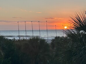 Ein Sonnenuntergang über dem Meer mit einem Strand im Vordergrund.