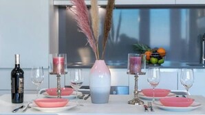 A dining table set with pink bowls, wine glasses, and a bottle of wine. There are decorative vases with pink and white flowers, and a fruit bowl with oranges and other fruits. - Villa Poco Loco -Comfort Two Bedroom Apartment (Dubrovačko-neretvanska županija)