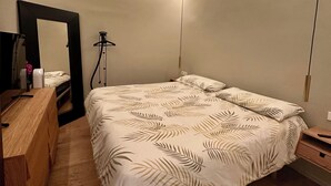 Quarto com cama, cómoda de madeira, espelho, ventoinha no teto e luminária pendente.
