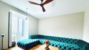 Uma sala de estar moderna com um sofá seccional verde-água, uma mesa de centro de madeira, um tapete vermelho e um ventilador de teto.