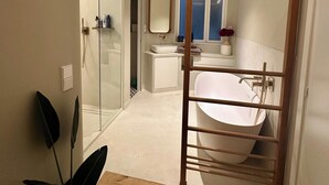 Um banheiro moderno com uma banheira de pés aparentes, box de vidro e uma escada de madeira que dá acesso ao chuveiro.