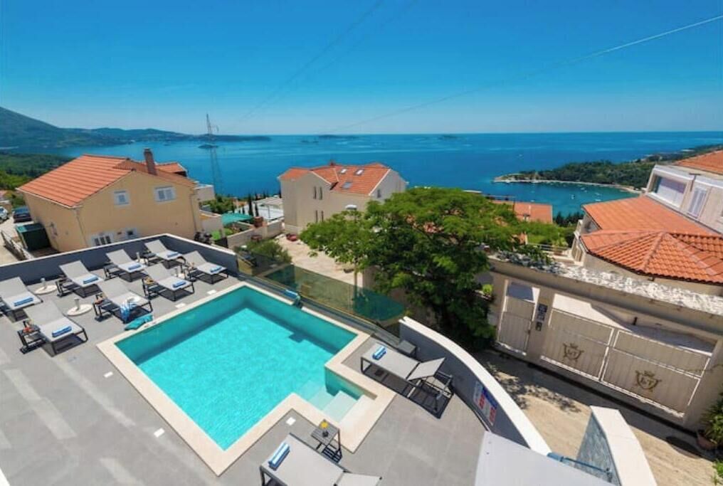 Una piscina en la azotea con sillones de descanso, vista al mar y edificios circundantes.