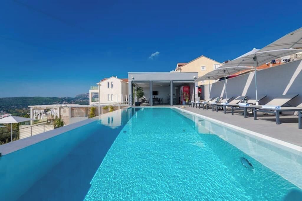 A rooftop infinity pool with lounge chairs and umbrellas, overlooking a scenic landscape.