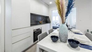 A modern kitchen with white cabinets, a black countertop, and a dining area with a white table set for two. - Villa Poco Loco - Deluxe Apartment with Sea View (Dubrovacko-neretvanska županija)