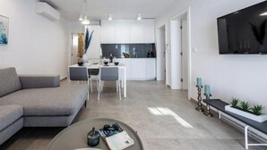 A modern living room with a grey sofa, a coffee table with magazines, and a TV mounted on the wall. - Villa Poco Loco - Deluxe Apartment with Sea View (Dubrovacko-neretvanska županija)