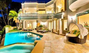 Un espace luxueux aménagé autour de la piscine, comprenant une grande piscine, des sièges extérieurs et un balcon bien éclairé.