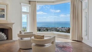 A spacious room with a large bay window offering a view of the sea and a town. There is a fireplace and two armchairs. - Private Pool/Spa/Open October/Sauna/Amazing La Jolla Views (La Jolla)