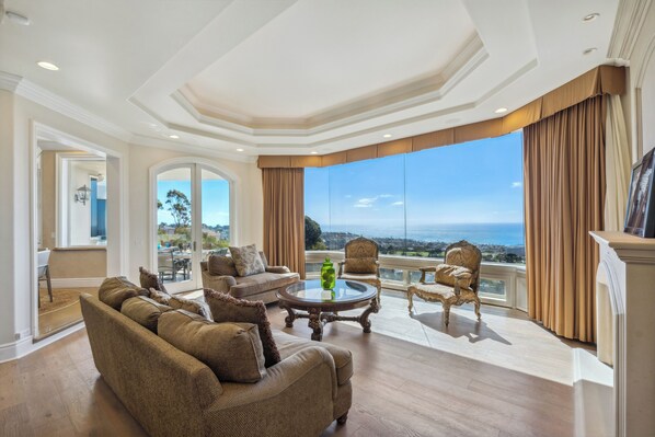 A spacious living room with a large window offering a view of the ocean, furnished with a sofa, armchairs, and a coffee table.