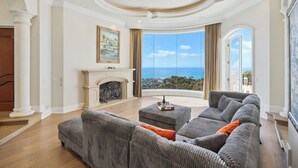 A spacious living room with a large gray sectional sofa, a fireplace, and a view of the ocean. - Private Pool/Spa/Open October/Sauna/Amazing La Jolla Views (La Jolla)