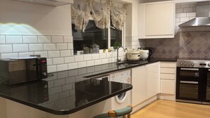 Una cocina moderna con encimera negra, armarios blancos, lavadora integrada y taburetes de madera.