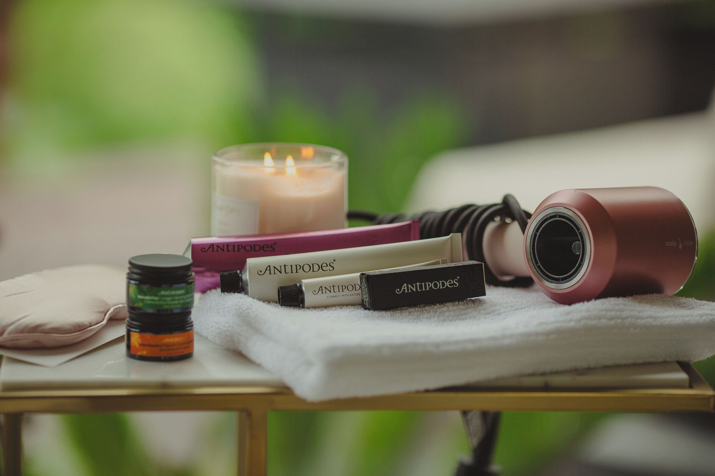 Uma mesa com produtos de cuidados para a pele, uma vela e um secador de cabelo.