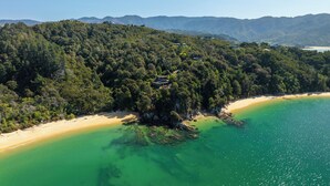 Vista aerea di una zona costiera con spiaggia, colline boscose e un piccolo edificio a picco sulla scogliera.