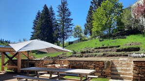 An outdoor patio with a stone wall, a wooden table, and a picnic table under a white umbrella. - Large apartment in village center with direct access to ski and hiking trails (Prémanon)