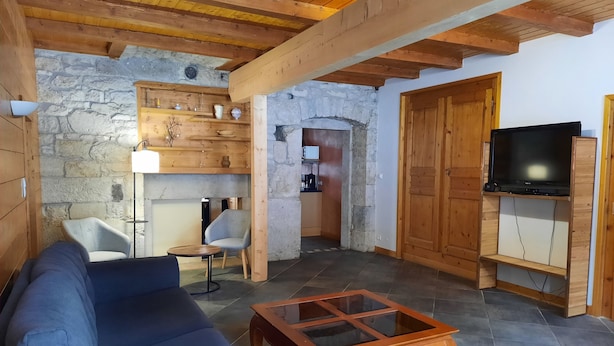A cozy living room with a sofa, a glass-top coffee table, a TV on a wooden stand, and a stone wall. - Large apartment in village center with direct access to ski and hiking trails (Prémanon)