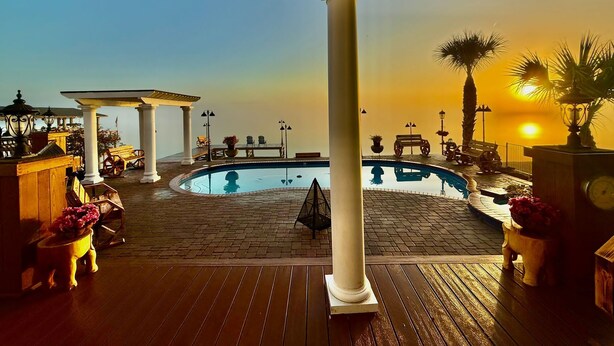 Un área de piscina con una pérgola, asientos y vistas al atardecer.