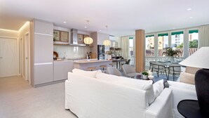 A modern living room with a white sofa, a dining area with a round table, and a kitchen with a central island.