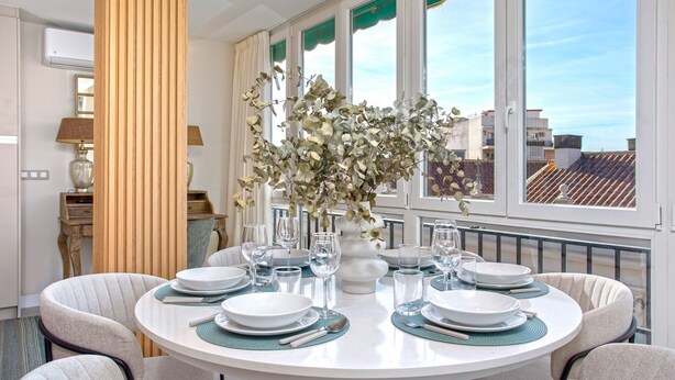 A round dining table set with plates, glasses, and a vase of flowers.