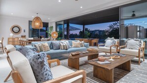 Un salon moderne avec un ensemble de canapés, une table basse en bois et des fauteuils. Une grande fenêtre offre une vue sur le paysage urbain.