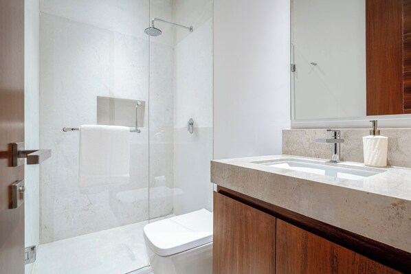 Un baño moderno con ducha acristalada, inodoro blanco y tocador con espejo.