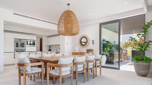 Une cuisine moderne avec des armoires blanches, des appareils en acier inoxydable et un coin repas comprenant une table et des chaises en bois.