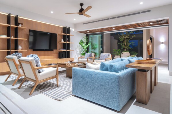 Una sala de estar moderna con un sofá, sillas, una mesa de centro y un televisor montado en la pared.