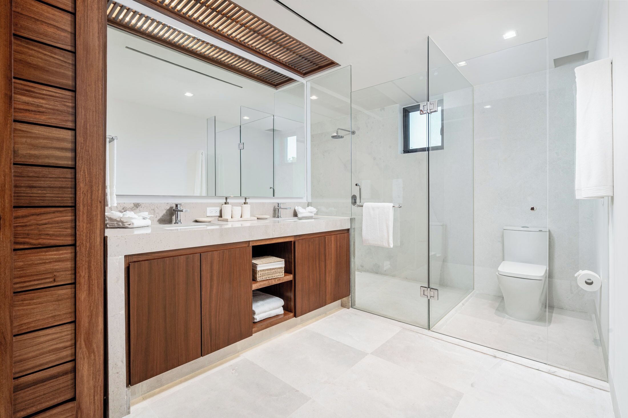 A modern bathroom with a wooden vanity, a glass-enclosed shower, and a large mirror.