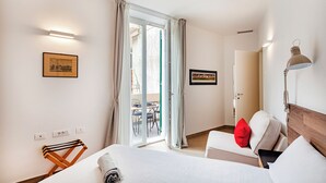A hotel room with a bed, a desk, a chair, a lamp, and a sliding glass door leading to an outdoor area. - Brignole de Ferrari Refined Home by Wonderful Italy (Genoa)