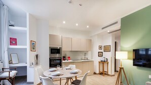 A modern kitchen with a built-in oven and microwave, a dining area with a round table and chairs, and a living area with a TV and floor lamp. - Brignole de Ferrari Refined Home by Wonderful Italy (Genoa)