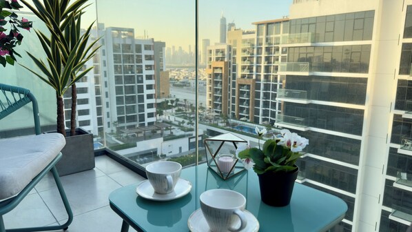 A balcony with a view of a cityscape, a chair, a table with cups and a potted plant. - Studio next Dubai Mall with pool (Dubai)