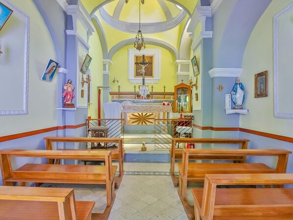 Ein Kircheninneres mit Holzbänken, einem zentralen Altar und religiösen Statuen.