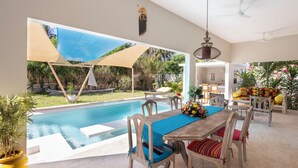 Un área de comedor junto a la piscina, con mesa y sillas, piscina y un espacio de descanso cubierto con vistas al jardín.