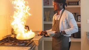 A chef cooking with a flame on a stove in a kitchen.