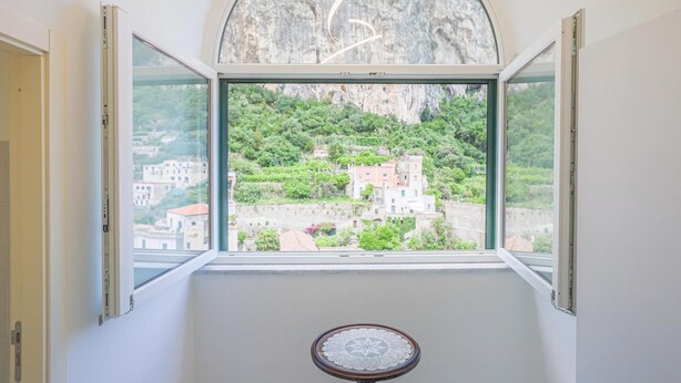 A room with a large arched window overlooking a hillside with buildings.