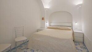 A bedroom with a bed, a bedside table, a chair, and a small wall-mounted shelf.