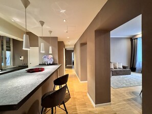 Una camera d'albergo moderna con angolo cottura, un tavolo da pranzo con sedie, un divano e un'ampia finestra.