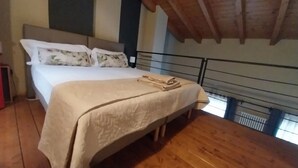 Ein Schlafzimmer mit Holzboden, einem Bett mit weißer Bettdecke und Kissen sowie einer Holzbalkendecke.