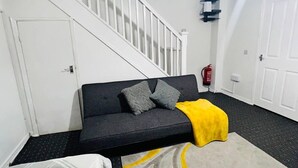 A modern living room with a sofa, a yellow throw blanket, and a staircase. - 3bedroom- Near to Station-private Garden-wifi (Liverpool)