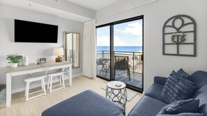 Een moderne woonkamer met een grote televisie, een balkon met uitzicht op zee en een gezellige zithoek.