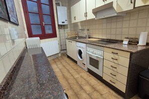 A kitchen with a built-in oven, a washing machine, and a window with a red frame.