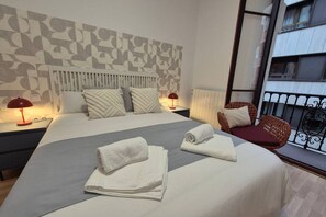 A hotel room with a bed, two bedside lamps, a chair, and a window with a view of a building.