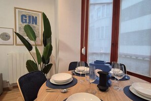 A dining table set with plates, glasses, and cutlery, with a view of a building through a window.