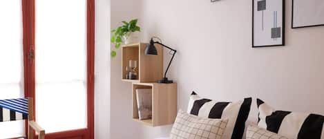 Un dormitorio con cama, almohadas, un escritorio con silla, un estante colgante con una planta y cuadros en la pared.
